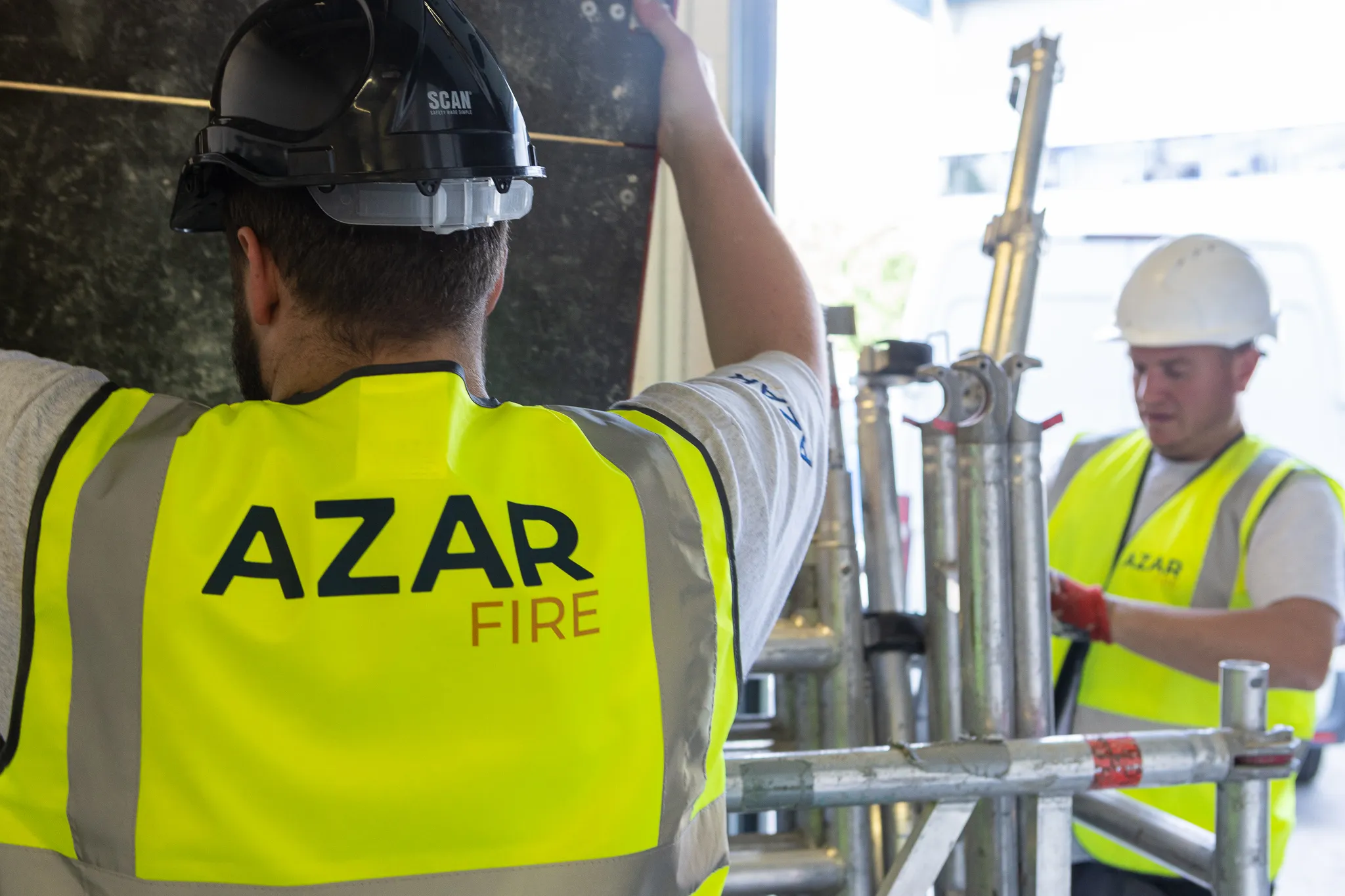 Two Azar Fire operatives in hi-vis erecting access scaffolding on site